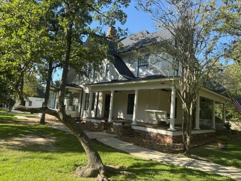 Side elevation of a repainted white two-storey farmhouse with a full-length covered porch