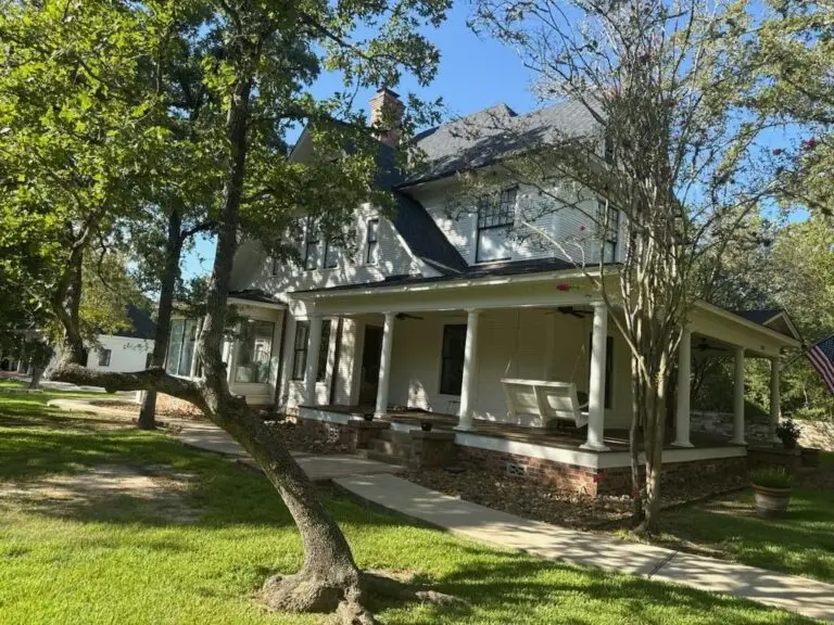 Side elevation of a repainted white two-storey farmhouse with a full-length covered porch
