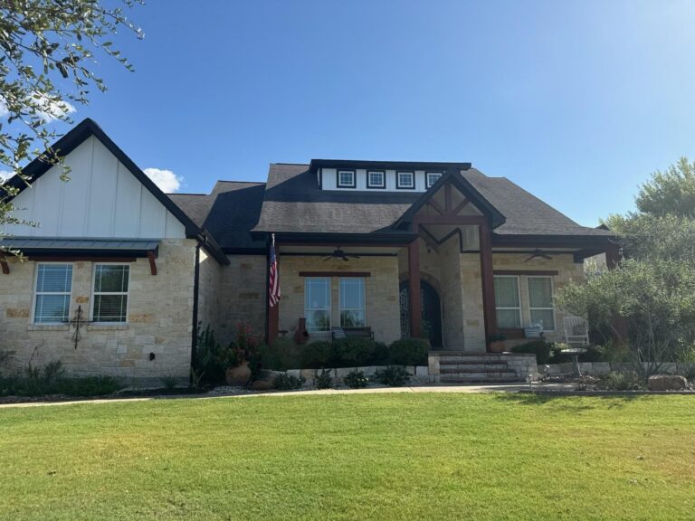 Modern stone and board-and-batten farmhouse with freshly painted trim, columns and a dark metal roof