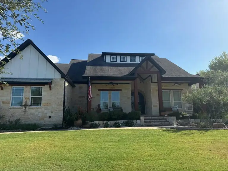 Modern stone and board-and-batten farmhouse with freshly painted trim, columns and a dark metal roof