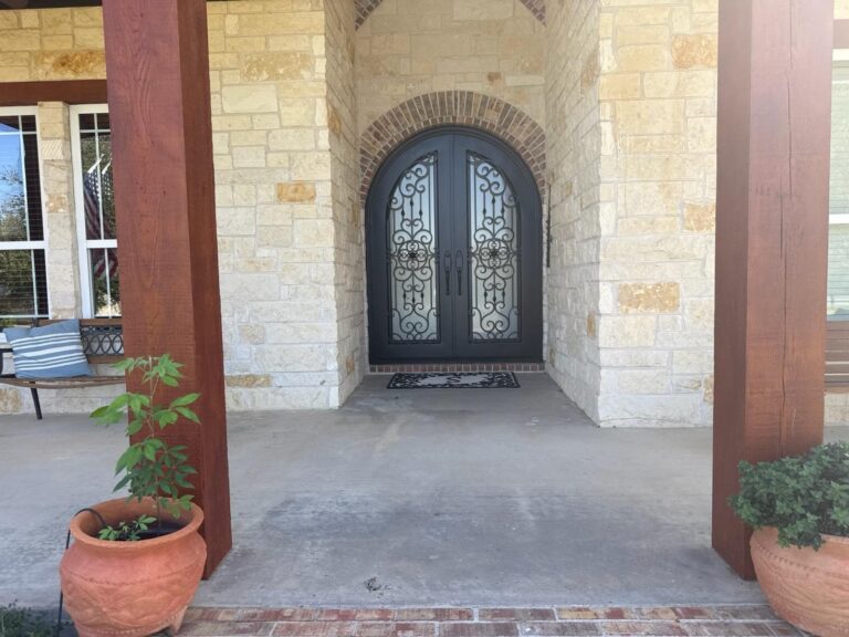 Arched wrought-iron double doors set in a stone entryway with painted timber columns